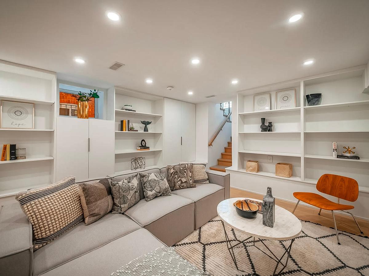 Finished basement with a modern living room featuring a modular sofa, built-in bookshelves, a marble coffee table, a wooden chair, and minimalist decor.