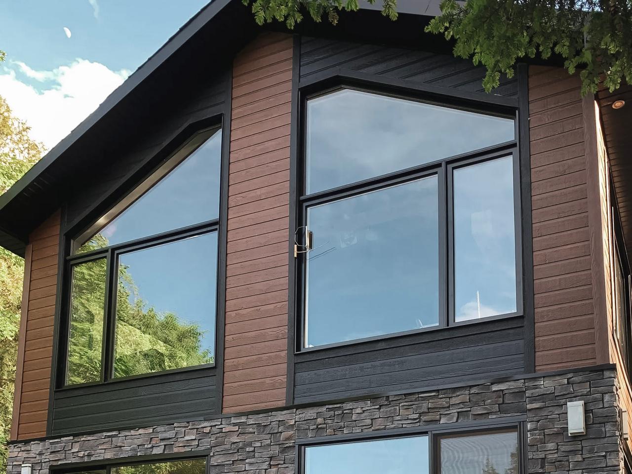 Modern house with wood siding, natural stone walls, large panoramic windows, and a wooden deck with a glass railing.