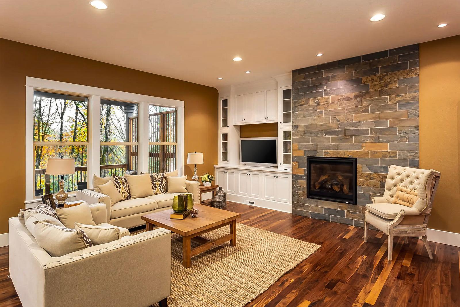 Cozy living room with a built-in stone fireplace, beige furniture, and large windows overlooking a terrace.