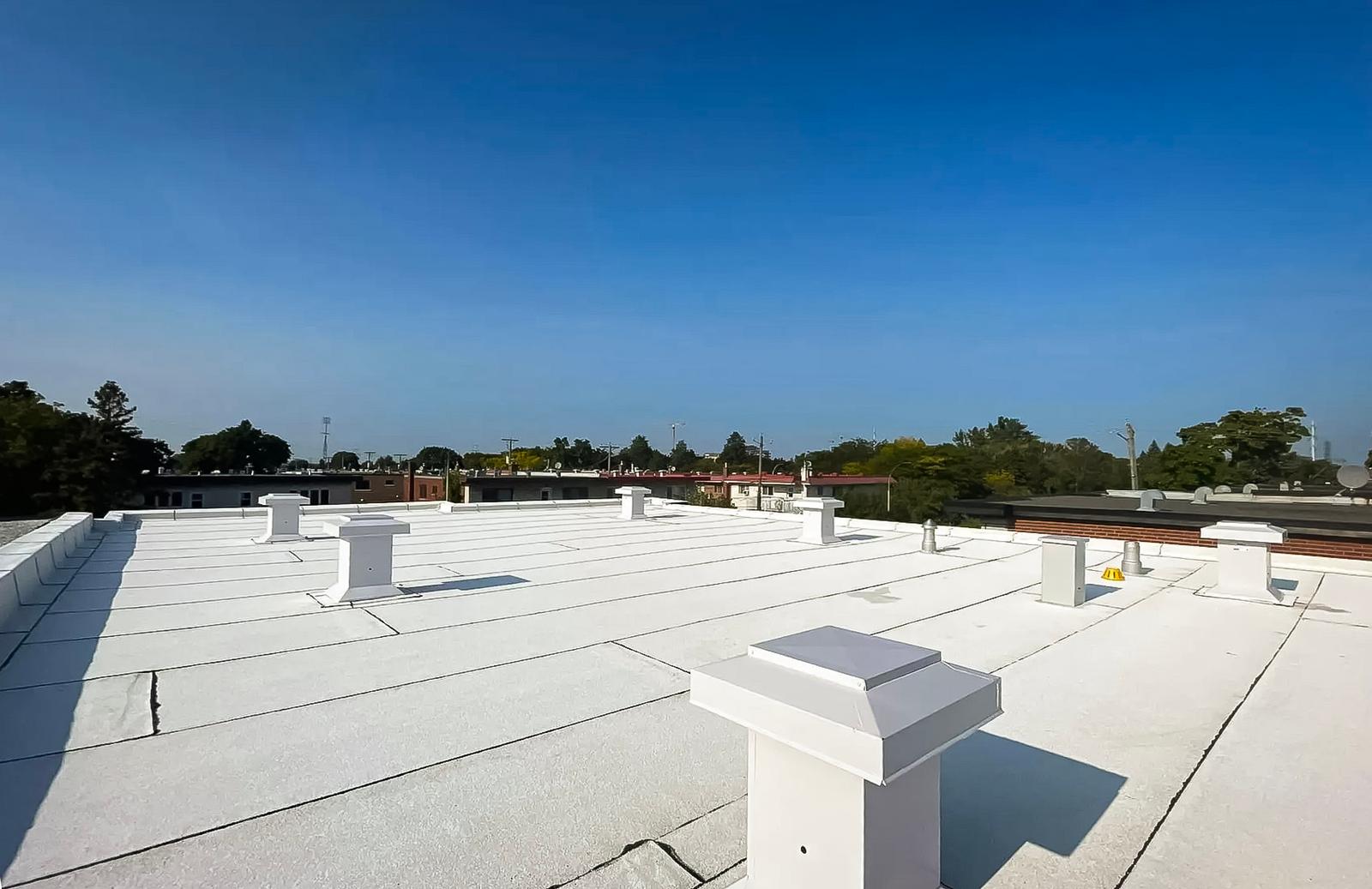 Flat roof covered with a white membrane featuring multiple ventilation vents under a clear sky.<br>