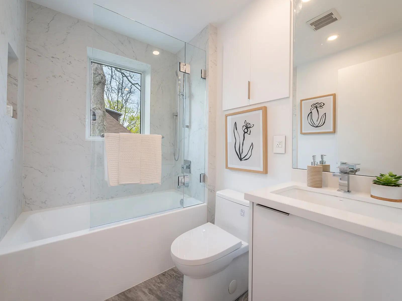 Modern bathroom with wood-look tiles, a white bathtub, glass shower, minimalist sink, wall-mounted cabinet, wall decor, indoor plants, and a zen ambiance