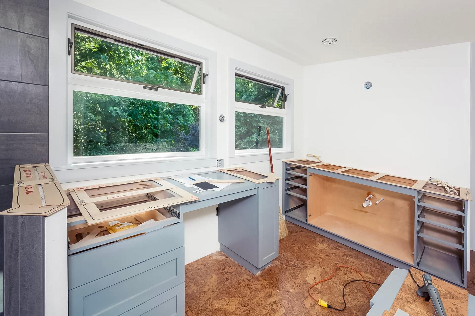 Kitchen under renovation with the installation of new countertops and gray cabinets under bright windows.