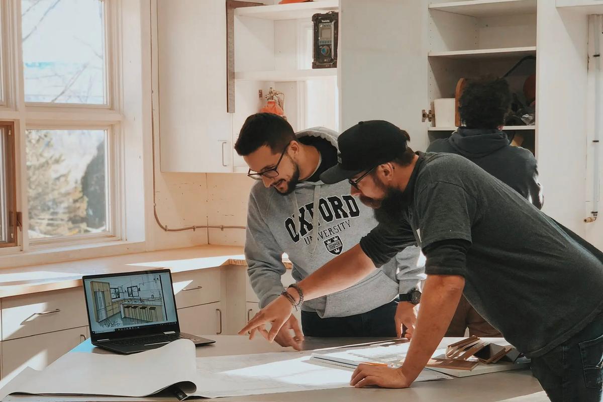 Professionals collaborating in a workshop on an architectural project design with plans and a laptop.