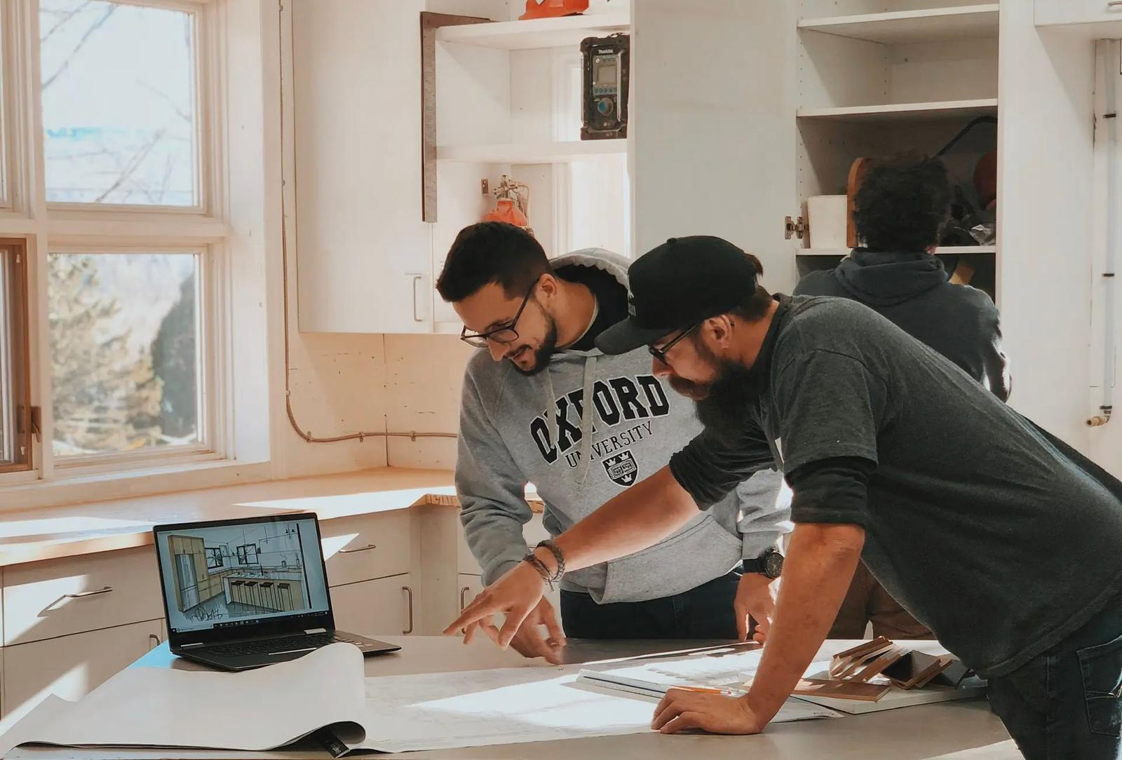 Professionals collaborating in a workshop on an architectural project design with plans and a laptop.
