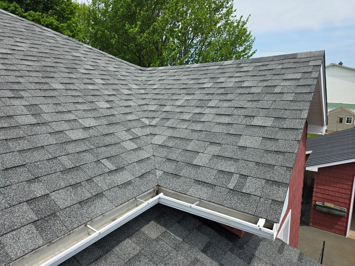 Gray asphalt shingle roof recently installed with white gutters on a red house.