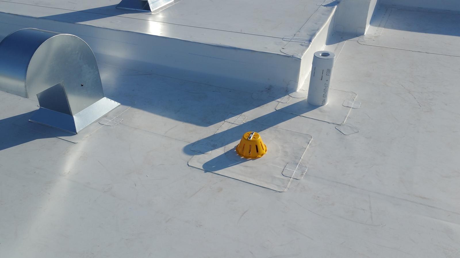 Flat roof with a white membrane, yellow roof drain, and ventilation elements for water and air drainage.