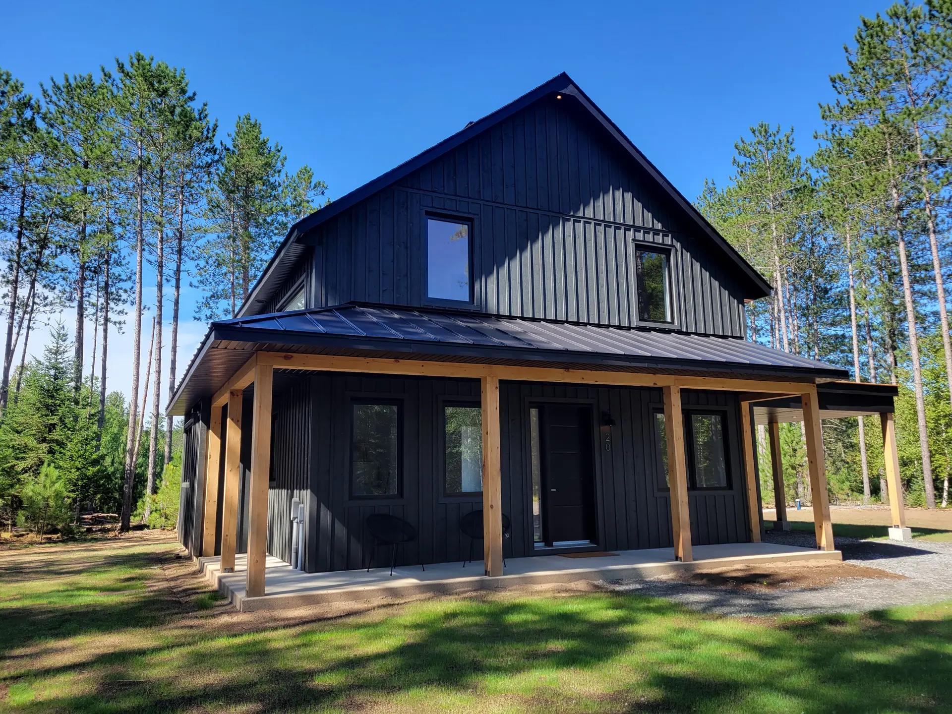 Modern home with metal roofing and wood beams, surrounded by tall trees, bathing in sunlight within natural woodlands.