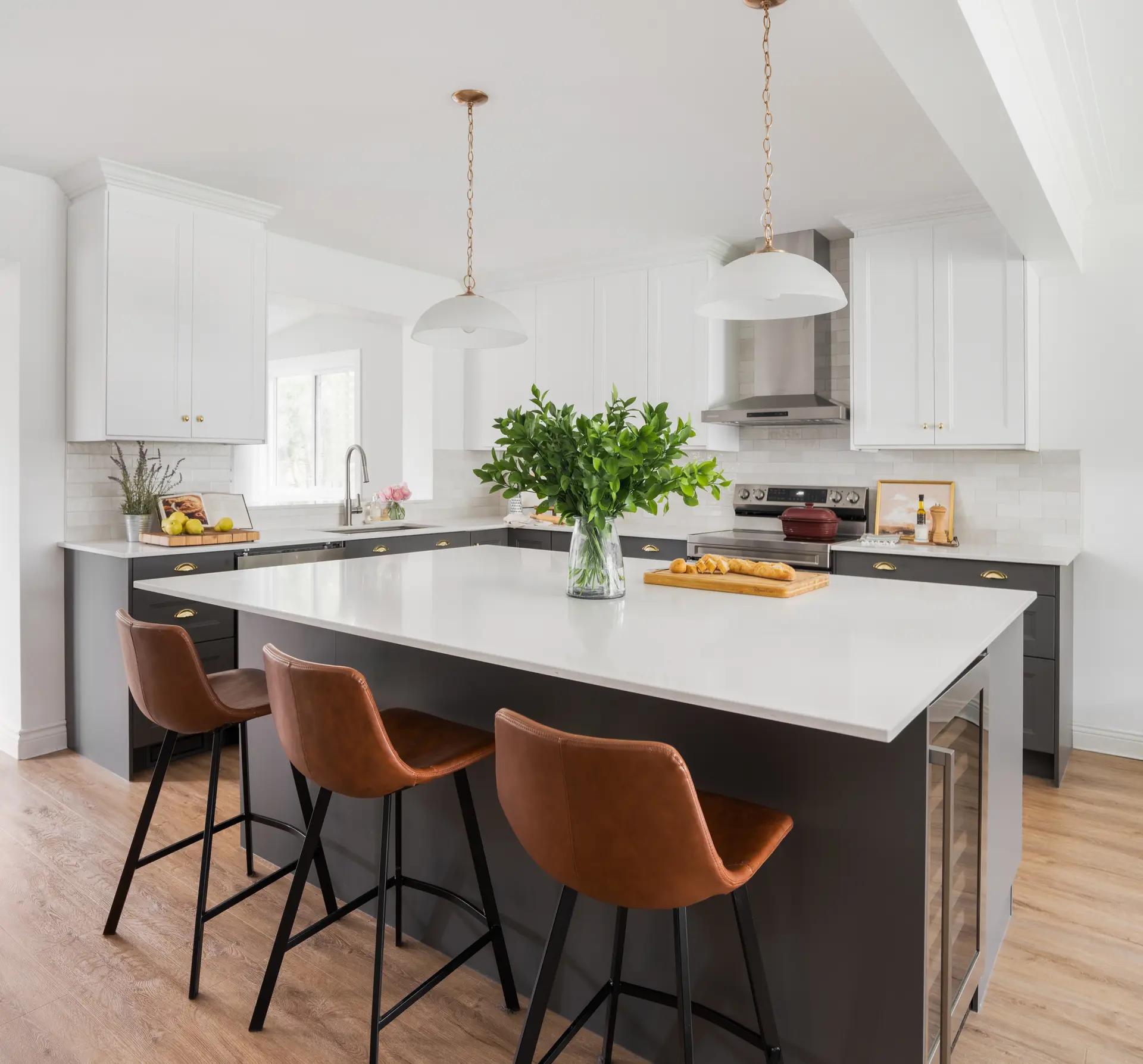 Transitional-looking Montréal kitchen, featuring a matte black central island with a white quartz countertop. The white shaker cabinets and copper handles add a touch of elegance to the space. The light wooden flooring and brown leather stools make for a warm, inviting setting.