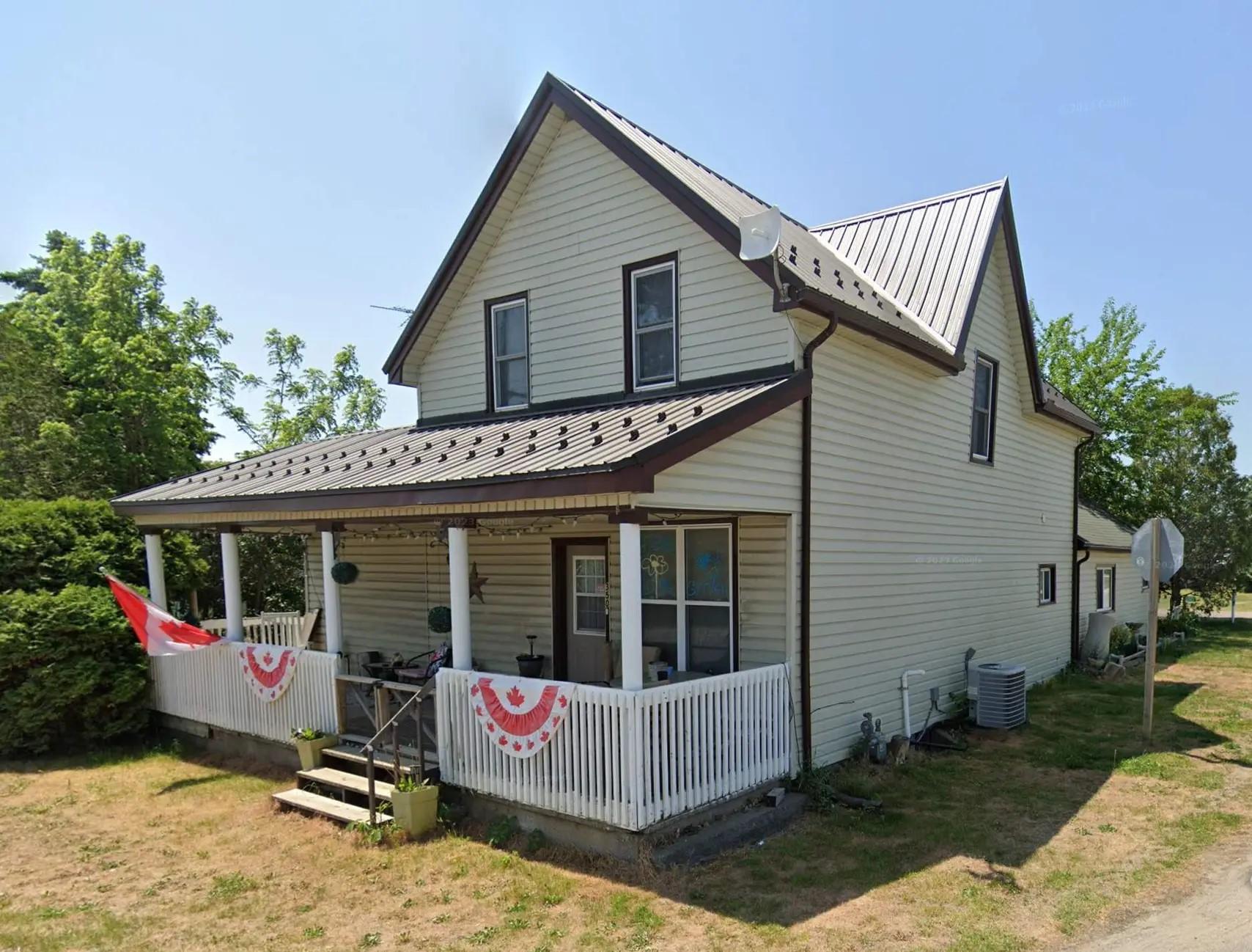 Two-story house decorated for Canada Day, with sheet metal roofing and a veranda located on a quiet residential street.