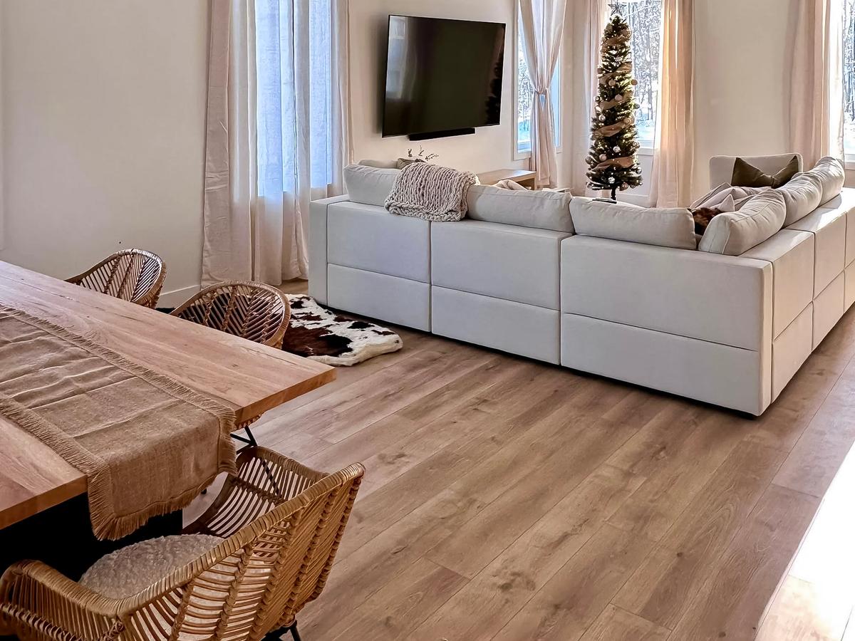 Bright living room with white sectional sofa, sheer beige curtains, wall-mounted TV, wooden dining table